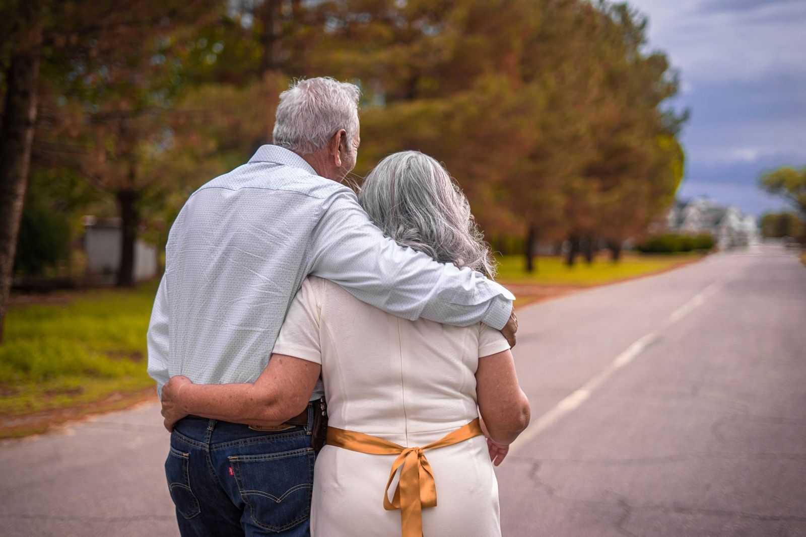 An older couple walking arm in arm down a tree-lined road
